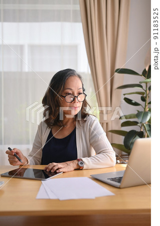 Focused middle aged woman wearing eyeglasses working at home with laptop, managing domestic bills and home finance 91183525