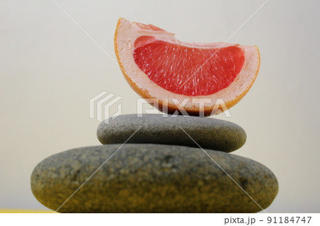 a ballans tower of grey stones and grapefruit orange fruit on a white yellow background with room for text. Benefits of Energy Health Importance Vitamin 91184747