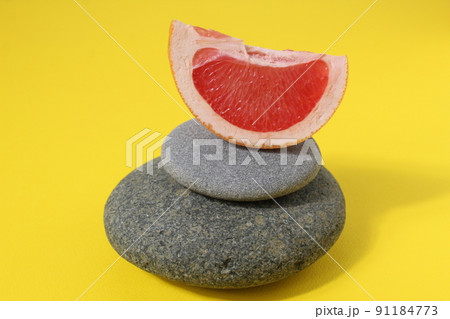 a ballans tower of grey stones and grapefruit orange fruit on a white yellow background with room for text. Benefits of Energy Health Importance Vitamin 91184773