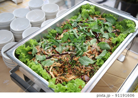 Larb Moo, sprinkled on top with mint leaves in buffet line. The container is a rectangular stainless steel tray with small white cups arranged on the side. Selective focus. Larb Moo, sprinkled on top with mint leaves in buffet line. The container is a rectangular stainless steel tray with small white cups arranged on the side. Selective focus. 91191606