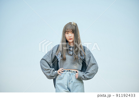 腰に手を当てて青空を背景に立つZ世代の女性 91192433