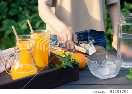 Girl cooking summer orange cocktail with mint and ice cubes outdoors, selective focus 91193702