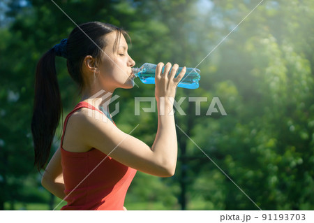 Beautiful young woman jogging in the morning in the park drinking blue isotonic from a bottle Beautiful young woman jogging in the morning in the park drinking blue isotonic from a bottle 91193703