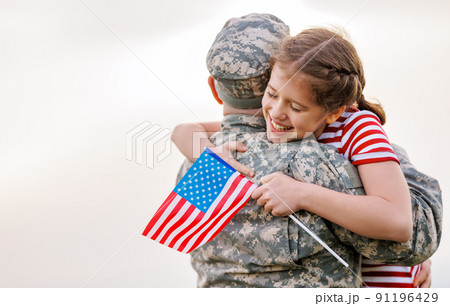 Happy girl daughter with american flag hugging father came back from US army Happy girl daughter with american flag hugging father came back from US army 91196429