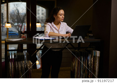 Beautiful Hispanic woman - creative and inspired interior designer works on a laptop in cozy home interior design studio Beautiful Hispanic woman - creative and inspired interior designer works on a laptop in cozy home interior design studio 91197217