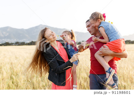 Happy family father of mother and two daughters sisters on nature at sunset.Carefree parents having fun with their kids on a field. Happy family father of mother and two daughters sisters on nature at sunset.Carefree parents having fun with their kids on a field. 91198601