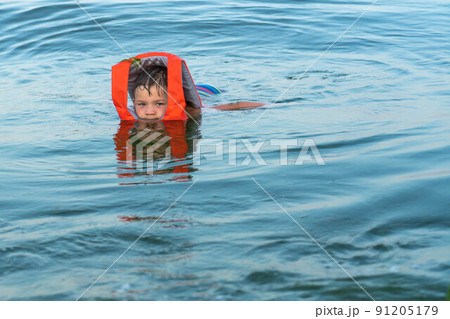A 5 year old boy is kept on the water in the sea with the help of a life jacket. 91205179