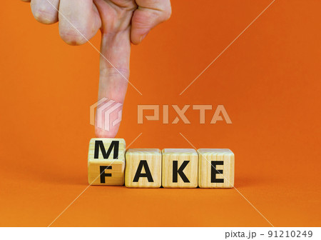 Fake it until you make it symbol. Businessman turns a wooden cube and changes the word Fake to Make. Beautiful orange background. Business, and fake it till you make it concept. Copy space. 91210249