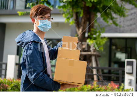 Asian postman with a hygiene protective face mask picking up a parcel package or parcel box from the truck for deliver to customer's door. New Normal concept during covid-19 or coronavirus pandemic Asian postman with a hygiene protective face mask picking up a parcel package or parcel box from the truck for deliver to customer's door. New Normal concept during covid-19 or coronavirus pandemic 91223671