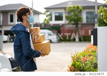 Asian postman with a hygiene protective face mask picking up a parcel package or parcel box from the truck for deliver to customer's door. New Normal concept during covid-19 or coronavirus pandemic Asian postman with a hygiene protective face mask picking up a parcel package or parcel box from the truck for deliver to customer's door. New Normal concept during covid-19 or coronavirus pandemic 91223675