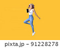 Full length portrait of young Asian woman holding smartphone jumping on yellow background 91228278