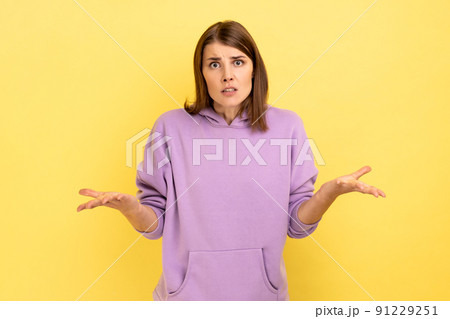 Portrait of dark haired woman raising hands and looking with confused expression, quarreling, annoyed by conflict, wearing purple hoodie. Indoor studio shot isolated on yellow background. Portrait of dark haired woman raising hands and looking with confused expression, quarreling, annoyed by conflict, wearing purple hoodie. Indoor studio shot isolated on yellow background. 91229251