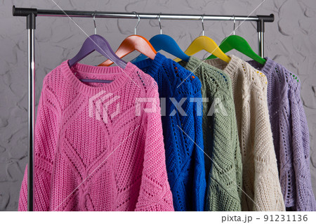 five sweaters of different colors, hung on a coat hanger, against a gray wall in a loft style 91231136