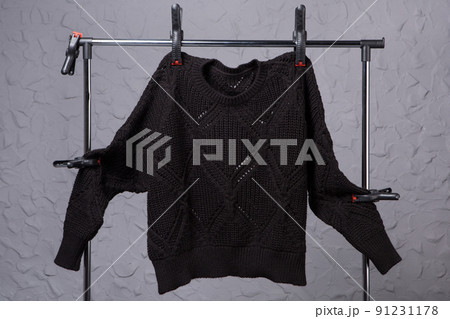 black knitted wool sweater, fastened with clothespins on a trade hanger, against a gray wall 91231178