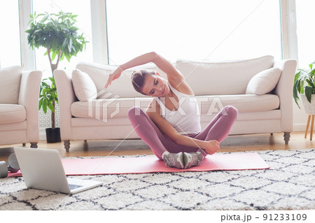 Cheerful woman doing fitness stretching exercises and using laptop at home.  91233109