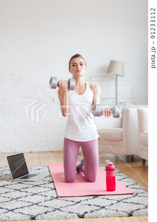 Healthy fit woman doing fitness exercises with dumbbells and using laptop indoor at home Healthy fit woman doing fitness exercises with dumbbells and using laptop indoor at home 91233112