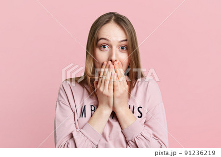 Attractive female covers mouth with hands as giggles or laughs, hears funny story from friend, isolated over pink background. Fashionable woman expresses positiveness, tries control her emotions 91236219