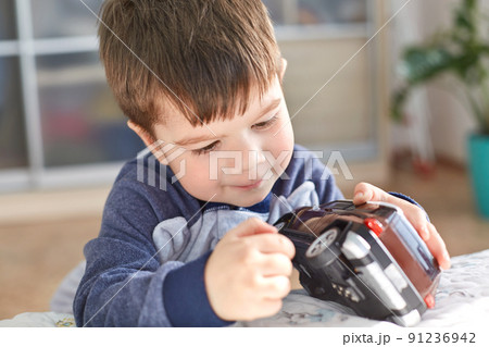 Indoor shot of good looking small kid holds toy car in hands, poses indoor against cozy domestic interior, likes to play with toys, has appealing look. Joyful cute boy preschooler being naughty 91236942