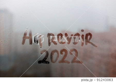 lettering Au revoir in French is goodbye in english and numbers 2022 paint with finger of water on splashed by rain foggy glass on sunset window lettering Au revoir in French is goodbye in english and numbers 2022 paint with finger of water on splashed by rain foggy glass on sunset window 91243063