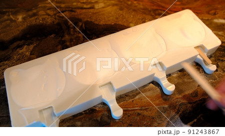 Making homemade popsicles. man pouring ice cream in freezer molds and put a stick inside Making homemade popsicles. man pouring ice cream in freezer molds and put a stick inside 91243867