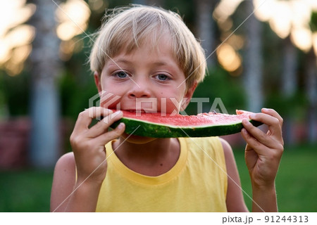Cute boy child eating healthy organic watermelon in garden, nature background, sunny lights Cute boy child eating healthy organic watermelon in garden, nature background, sunny lights 91244313