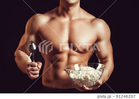 Strong, healthy man posing on a black background. Bodybuilder, athlete eats cottage cheese . The concept of a healthy diet and a healthy lifestyle 91246207