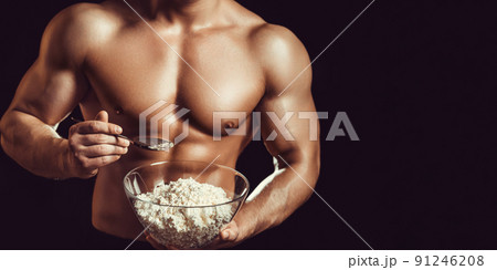 Strong, healthy man posing on a black background. Bodybuilder, athlete eats cottage cheese . The concept of a healthy diet and a healthy lifestyle 91246208