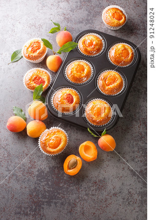 Delicious golden muffins with ripe apricots close-up in a muffin pan. Vertical top view 91248024