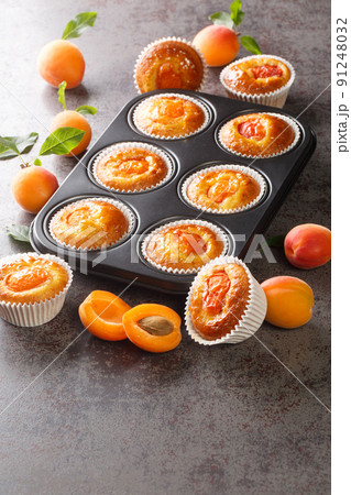 Freshly baked summer muffins with fresh apricots close-up in a muffin pan. Vertical Freshly baked summer muffins with fresh apricots close-up in a muffin pan. Vertical 91248032