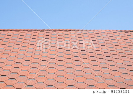 New roof with red shingles against the blue sky. High quality photo. Tiles on the roof of the house. Use to advertise roof fabrication and maintenance. Spotted texture. Affordable roofing. 91253131