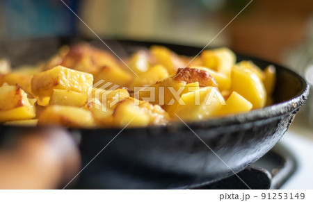Roasting fresh potatoes in a cast iron skillet with sunflower oil. A view of a stovetop with a frying pan filled with golden fried potatoes in a real kitchen. Food cooked in a homemade frying pan. 91253149