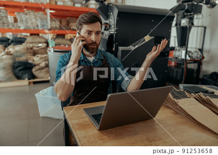 Handsome man make business talking phone on own small coffee factory Handsome man make business talking phone on own small coffee factory 91253658