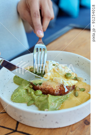 Young woman eat breakfast with knife and fork, Morning in cafe. Healthy breakfast with wholemeal bread toast with avocado, poached egg with green salad. Young woman eat breakfast with knife and fork, Morning in cafe. Healthy breakfast with wholemeal bread toast with avocado, poached egg with green salad. 91254018