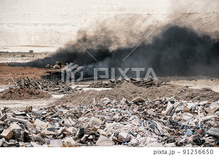 Fire at garbage dump, black smoke from burning old tyres and bulldozer fighting fire. 91256650