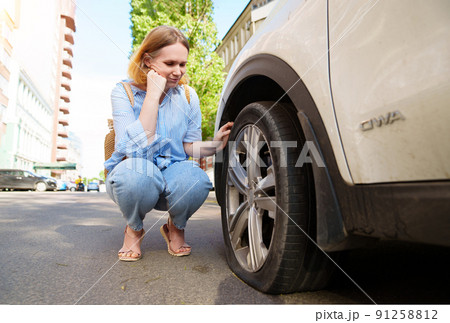 a sad woman sits at the punctured wheel of a car. tire service. solar glare a sad woman sits at the punctured wheel of a car. tire service. solar glare 91258812