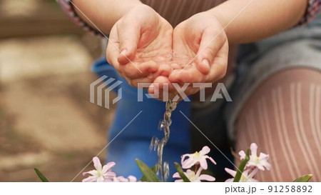 a little girl watering flowers from the palms of her hands. 91258892