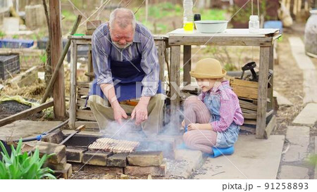 granddaughter helps grandfather cook barbecue 91258893