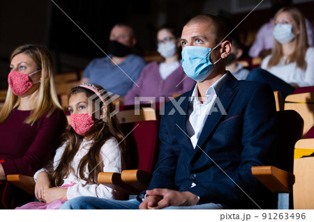 Family with child wearing protective masks eating popcorn and watching a movie in cinema Family with child wearing protective masks eating popcorn and watching a movie in cinema 91263496
