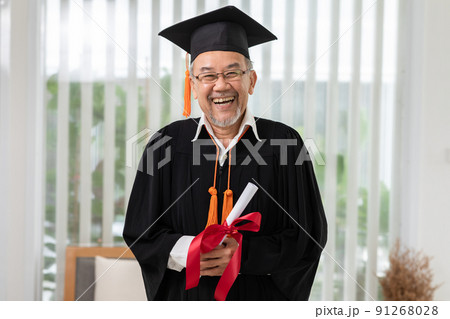 Asian elderly in cap and gown smile and celebration proud success graduate. Cheerful senior man holding certificated or diploma glad and happiness. Elderly graduation concept 91268028