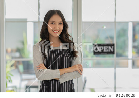 Happy Asian young business owner woman standing amile and cross arm in coffee shop cafe with open label in background. Cheerful of confident entrepreneur female looking at camera. Small business 91268029