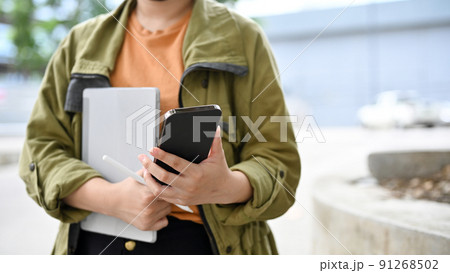 A hipster female standing in the park, holding a portable tablet and using smartphone. 91268502