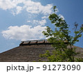 青空と白い雲と藁ぶきの屋根と新緑の木々 91273090