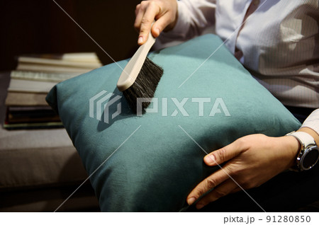 Close-up. Woman's hands cleaning a velour pillow from dust. General house cleaning, professional furniture cleaning, cleaning company concept Close-up. Woman's hands cleaning a velour pillow from dust. General house cleaning, professional furniture cleaning, cleaning company concept 91280850