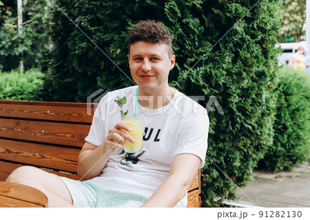 Young caucasian man with glass of lemonade in outdoor cafe, having brunch on sunny day. Portrait, cocktail. Young caucasian man with glass of lemonade in outdoor cafe, having brunch on sunny day. Portrait, cocktail. 91282130