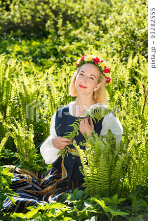 Young woman in national clothes and wreath against the background of a green fern. Ligo Latvian holiday 91282555