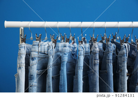 Rack with stylish jeans on blue background, closeup 91284131