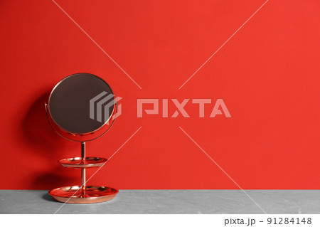 Small mirror on grey marble table near red wall. Space for text 91284148