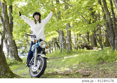 バイク女子イメージ　森でバイクのステップの上に立って万歳をする若い女性 91284176
