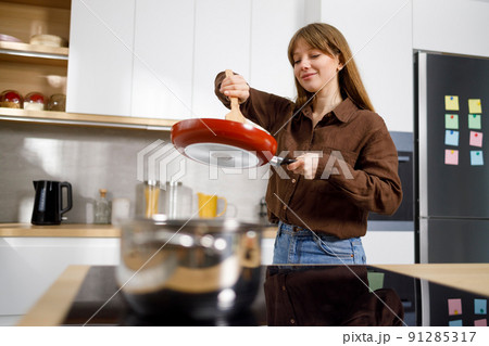 Young woman at the stove stirring food in a frying pan with a spatula. Housewife cooks in the kitchen Young woman at the stove stirring food in a frying pan with a spatula. Housewife cooks in the kitchen 91285317