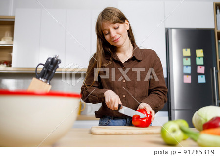 Young woman cutting paprika in the kitchen. Housewife preparing food Young woman cutting paprika in the kitchen. Housewife preparing food 91285319